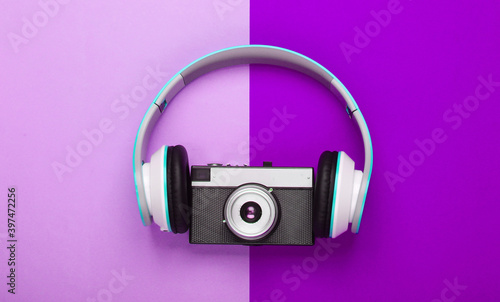 Stylish stereo headphones with retro camera on purple background. Music lover. Travel concept. Retro 80s. Top view.