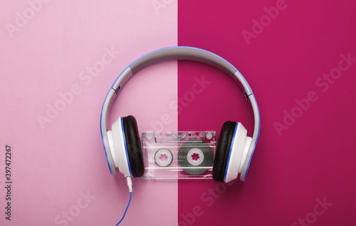 Stylish wired stereo headphones with audio cassette on red pink background. Music lover. Retro 80s. Top view.