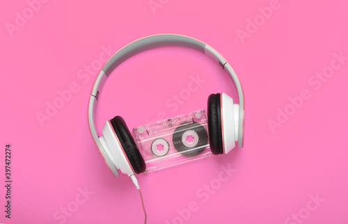 Stylish wired stereo headphones with audio cassette on pink background. Music lover. Retro 80s. Top view.