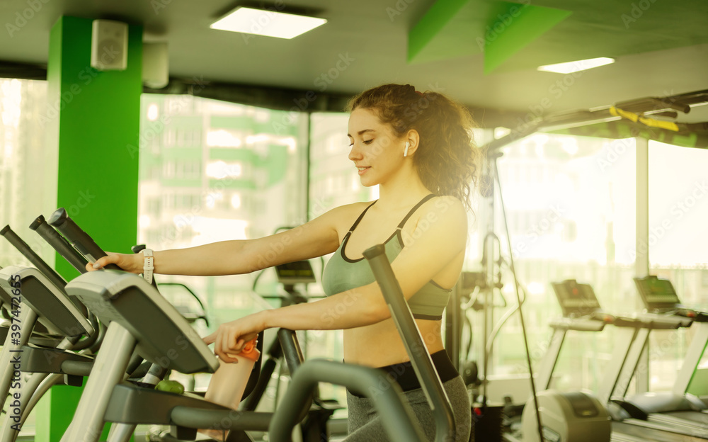 Young attractive woman warming up on an elliptical exercise machine in the gym. Fitness, healthy lifestyle concept. Young attractive woman warming up on an elliptical exercise machine in the gym. Fitness, healthy lifestyle concept.