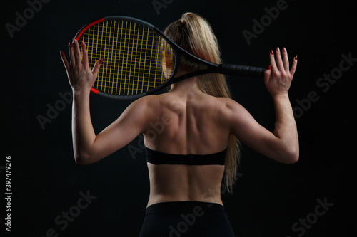 Beautiful athletic blonde girl tennis player holding a racket behind her back isolated on a black background view from the back. © ksi