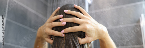 Woman stands under shower and washes her hair. Evening showering and fatigue relief concept photo