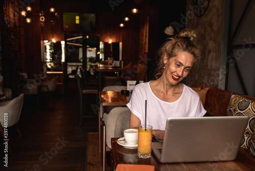 Smiling senior female blogger in casual wear sitting in coffee shop using laptop.