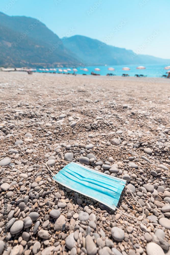Used medical mask discarded on a sandy beach by the sea. The concept of irresponsible behavior and environmental pollution. Another social problem of the coronavirus epidemic. Used medical mask discarded on a sandy beach by the sea. The concept of irresponsible behavior and environmental pollution. Another social problem of the coronavirus epidemic.