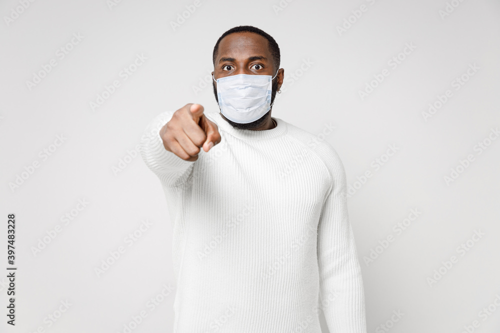 Young african american man in basic sweater sterile face mask safe from coronavirus virus covid-19 during quarantine pointing index finger on camera isolated on white color background studio portrait. Young african american man in basic sweater sterile face mask safe from coronavirus virus covid-19 during quarantine pointing index finger on camera isolated on white color background studio portrait.