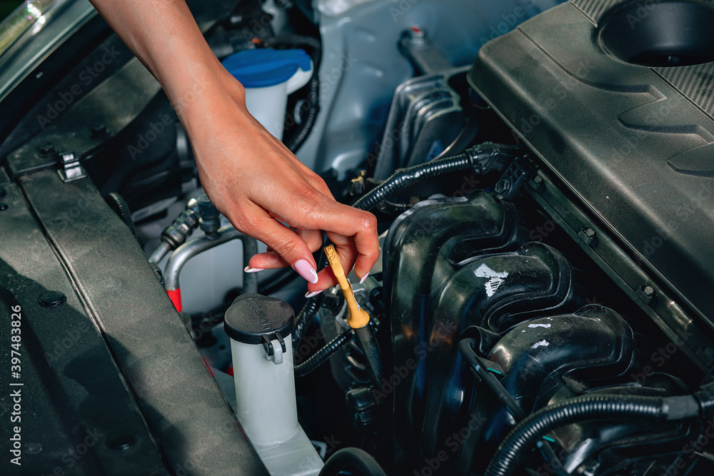 Fototapeta premium girl's experienced gentle hand is checking an oil dipstick in her car, close up