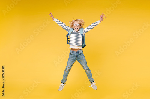 Full length of excited male boy 10s years old in striped sweatshirt eyeglasses backpack jumping spreading hands and legs isolated on yellow color background child studio portrait. Education concept.