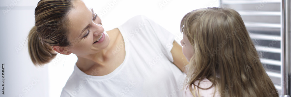 Young woman mother looking at baby and smiling in bathroom portrait. Daily morning hygiene procedures for children concept. Young woman mother looking at baby and smiling in bathroom portrait. Daily morning hygiene procedures for children concept.