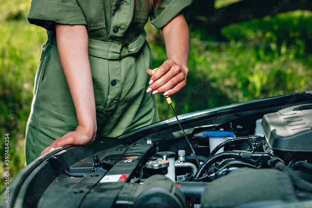 woman's experienced hand is checking an oil in the car via an oil dipstick against the background of nature, close up woman's experienced hand is checking an oil in the car via an oil dipstick against the background of nature, close up