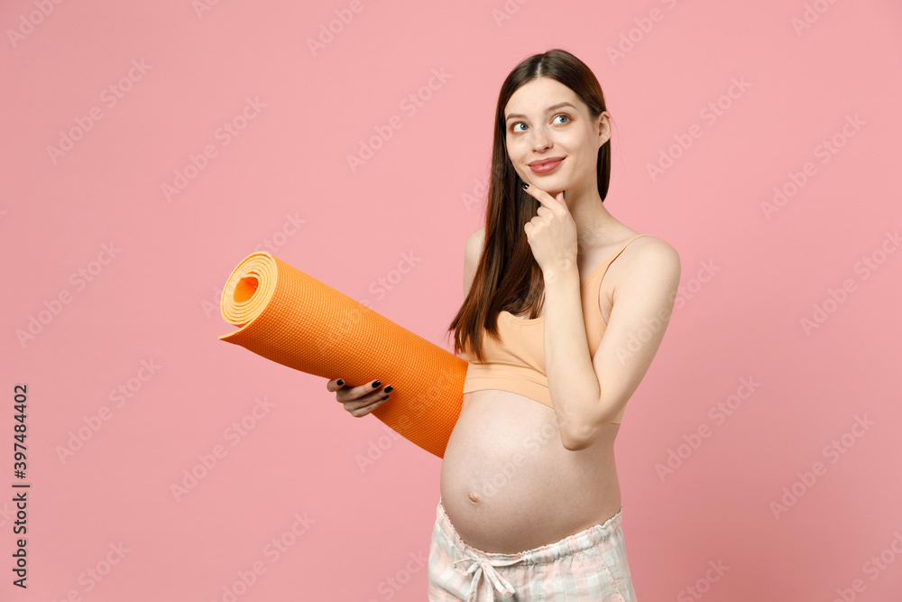 Young strong sporty fitness pregnant woman keeping hands on big belly stomach tummy with baby hold yoga mat isolated on pastel pink background studio. Maternity family pregnancy expectation concept Young strong sporty fitness pregnant woman keeping hands on big belly stomach tummy with baby hold yoga mat isolated on pastel pink background studio. Maternity family pregnancy expectation concept