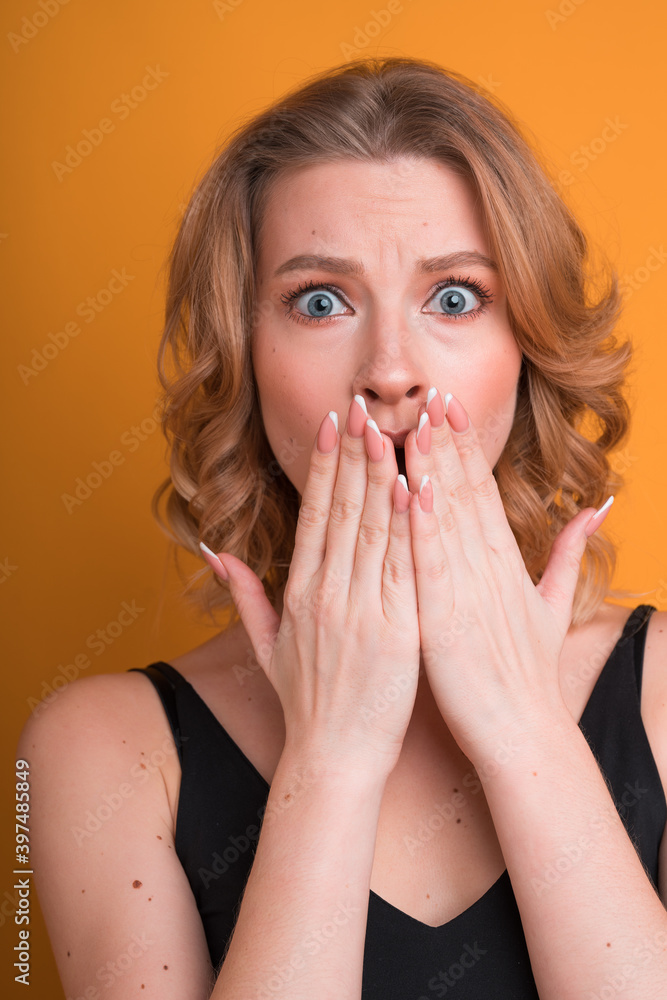 Shocked blonde American girl covering her mouth with her hands with a natural manicure. Feelings and emotions concept Shocked blonde American girl covering her mouth with her hands with a natural manicure. Feelings and emotions concept