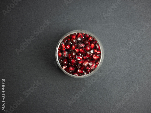 glass containing juicy pomegranate seeds, on dark slate background, still life fruit top view