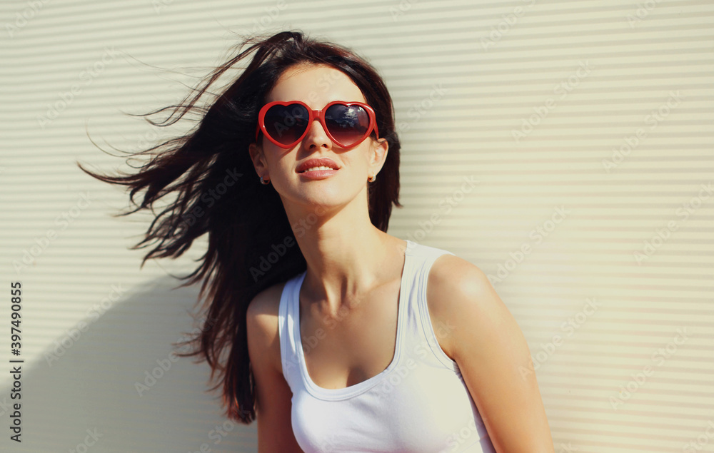Close up portrait of young woman wearing a red heart shaped sunglasses over a white background Close up portrait of young woman wearing a red heart shaped sunglasses over a white background