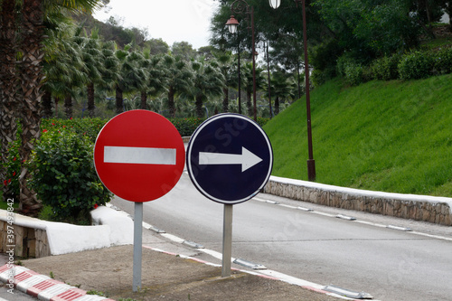 two different road signs in a countryside street with green palms trees 