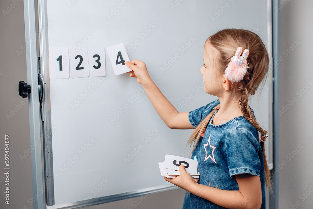 Little cute puppet girl child arranging numbers in the correct order. Beautiful child holding a card with number 4. Concept of mathematics. photo with noise.