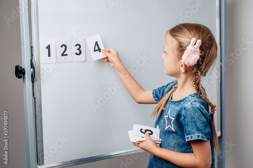 Obraz na płótnie Little cute puppet girl child arranging numbers in the correct order. Beautiful child holding a card with number 4. Concept of mathematics. photo with noise. w salonie