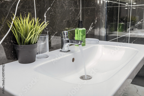 Close up a beautiful snow-white sink with soap  an artificial flower and glassware in a matte bathroom