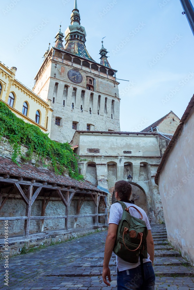 Back view of man looking on the citadel, located in the historic region of Transylvania. Clock tower or tower of the Town Hall and medieval architecture in the center of Sighisoara in Romania. 