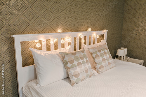 Close up soft white beautiful bed with beautiful square pillows and lamps standing in a room with green wallpaper