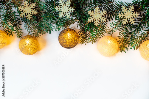 Branches of spruce with glowing baubles lying on the Christmas background. White background with shiny snowflakes.