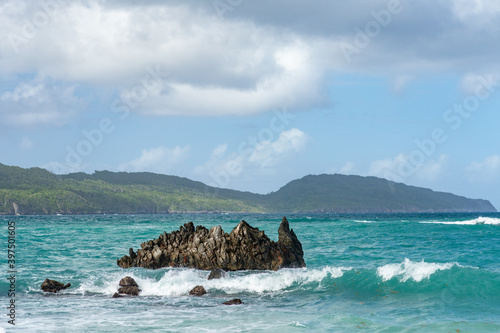 Lone coral rock in blue water of Atlantic Ocean with green mountains at the background, Rincon, Samana, Dominican Republic 