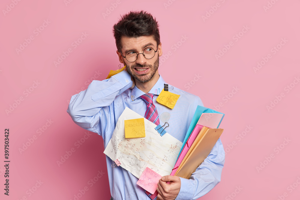 Tired exhausted employee has neckpain holds folders and wears shirt with attached sticky notes written information poses against pink background. Fatigue student studies hard before final exam Tired exhausted employee has neckpain holds folders and wears shirt with attached sticky notes written information poses against pink background. Fatigue student studies hard before final exam