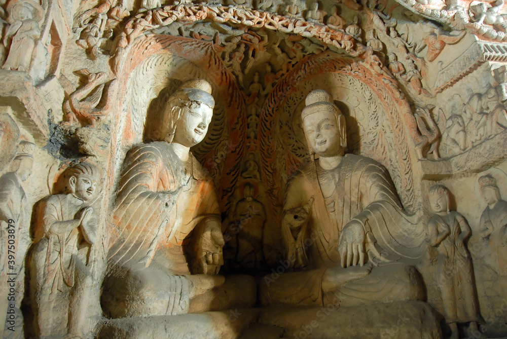 Yungang Grottoes near Datong in Shanxi Province, China. Two seated figures in a cave at Yungang. Surrounded by smaller carvings. Yungang Buddhist cave art and sculptures UNESCO world heritage.