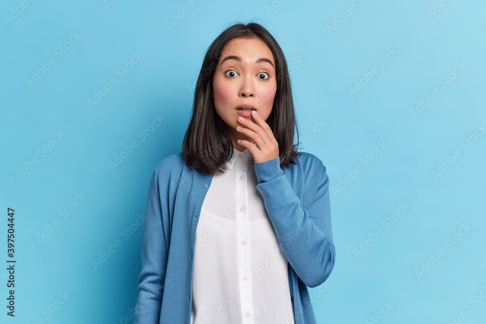 Impressed beautiful woman looks with great wonder keeps eyes widely dressed in neat clothing poses against blue background. Human face expressions and emotions concept. Extremely surprised female Impressed beautiful woman looks with great wonder keeps eyes widely dressed in neat clothing poses against blue background. Human face expressions and emotions concept. Extremely surprised female