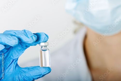 Doctor's Hand in blue gloves hold the vial with vaccine or drug