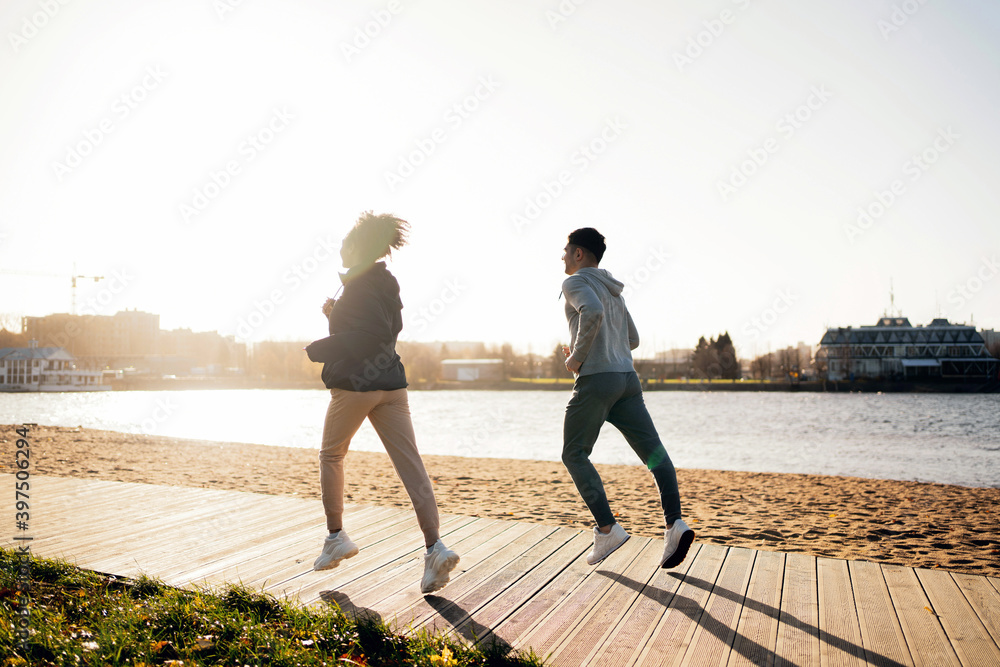 Run along the embankment in the city center. Healthy lifestyle, comfortable sportswear, beautiful sunset. young couple athletes man and woman doing sports fitness on the street in the autumn.
