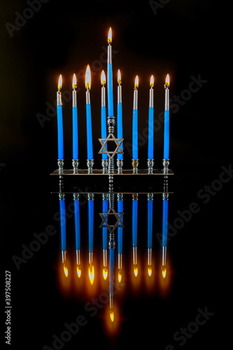 Vertical menorah with blue candles and reflection on surface for Hanukkah jewish holiday.