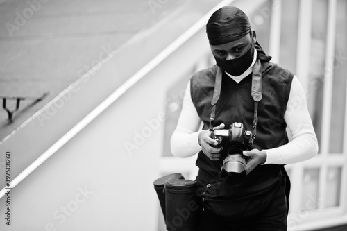 Young professional african american videographer holding professional camera with pro equipment. Afro cameraman wearing black duraq and face protect mask, making a videos. photo