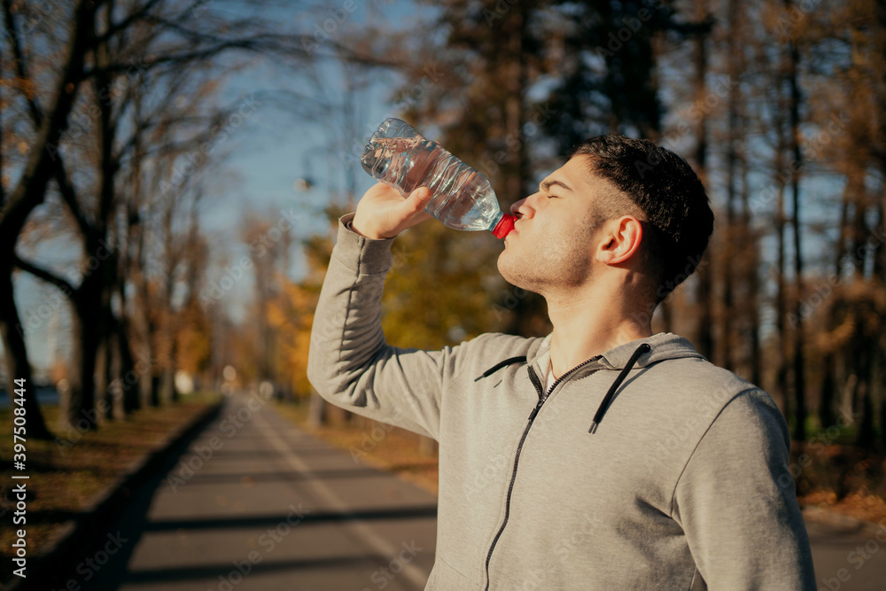an athlete drinks water after a workout in the Park. a young man is playing sports on the street an athlete drinks water after a workout in the Park. a young man is playing sports on the street