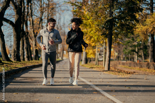 Fototapeta Naklejka Na Ścianę i Meble -  running in the Park friends trainers with each other. A man and an African American woman in sports comfortable clothing for aerobics fitness training in a Park in the city. the pair are engaged