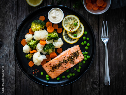 Steamed salmon steak with cauliflower, broccoli, carrots, lemon, peas and mayonnaise on wooden table 