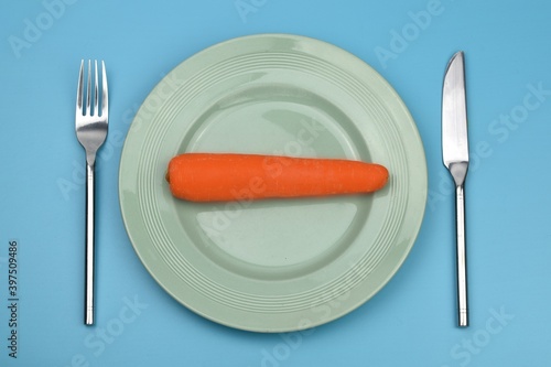  carrot in a plate with knife and fork on blue background 