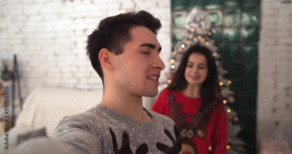 Close-up. The young man is talking in a video call, followed by a girl who approaches him hugging Close-up. The young man is talking in a video call, followed by a girl who approaches him hugging