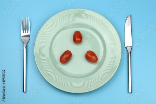 cherry tomatoes on a plate with knife and fork on blue background 