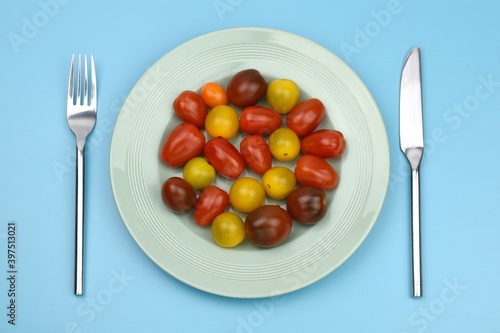  tomatoes on a plate with knife and fork on blue background 