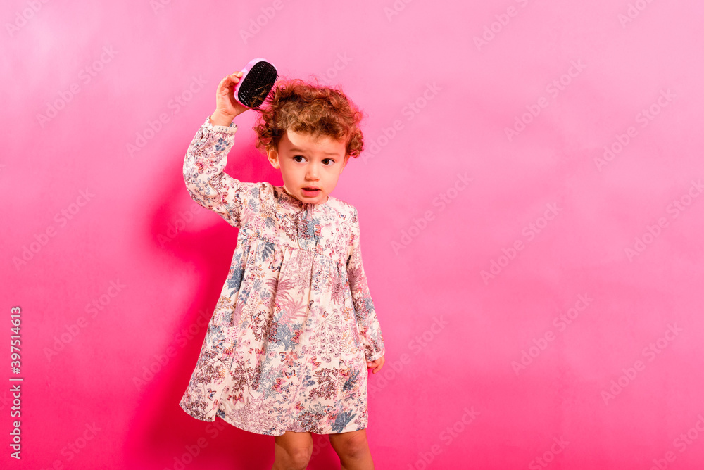 Two year old girl brushing her tangled hair, adorable, isolated on studio background.