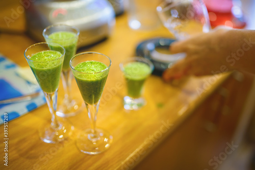 Four small glasses with spinach smoohie on the kitchen counter.