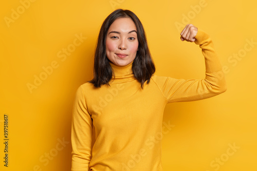 Fotografia Serious self confident brunette young Asian woman raises hand up and shows demon