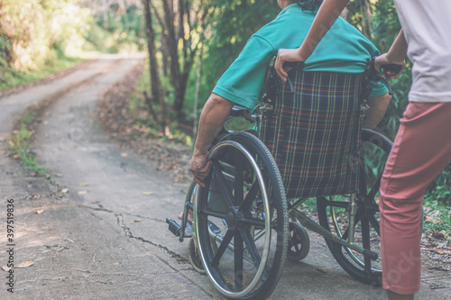 disabled handicapped man in wheelchair and care helper walking in park.