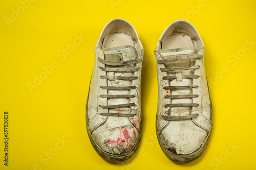 Dirty shoes, vintage white torn sneakers isolated on a yellow background.