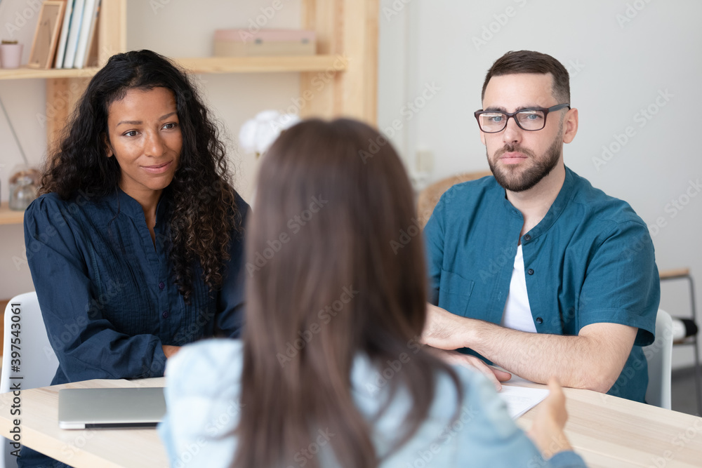 Obraz premium Serious diverse recruiters listen to female job applicant speak at interview in office. Multiracial man and woman employers have recruitment talk with work candidate applying. Employment concept.
