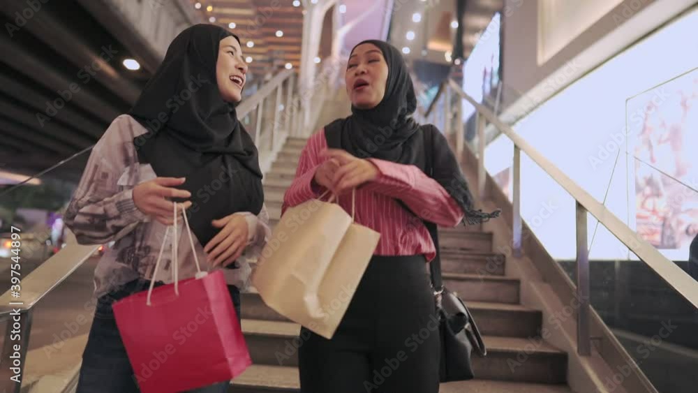 Two asian muslim females walking down the stairs at community shopping mall, girls spending money at the end of the month, customer member consumer buying habit, show off shopping bag, sales discount Two asian muslim females walking down the stairs at community shopping mall, girls spending money at the end of the month, customer member consumer buying habit, show off shopping bag, sales discount