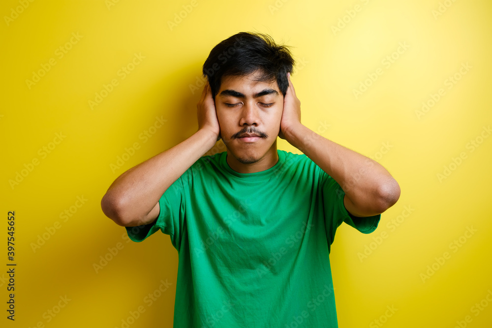 Asian young man in green t-shirt close his ears with both hands Asian young man in green t-shirt close his ears with both hands