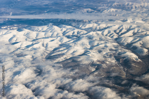 Snowy mountains from a bird's eye view on a clear blue sky with clouds. © Evgeniy