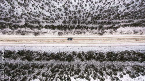  the car moves quickly along a sandy, icy road that passes through a young forest