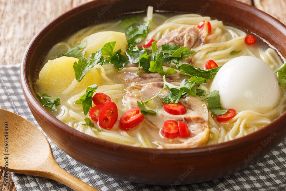 South American Caldo de Gallina chicken noodle soup with boiled egg and herbs close-up in a plate on the table. horizontal South American Caldo de Gallina chicken noodle soup with boiled egg and herbs close-up in a plate on the table. horizontal
